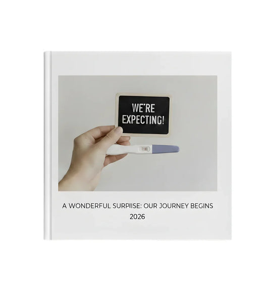 White Pebble photo book cover showing a hand holding a pregnancy test and sign reading 'We're Expecting', with the title 'A Wonderful Surprise: Our Journey Begins 2026' below.